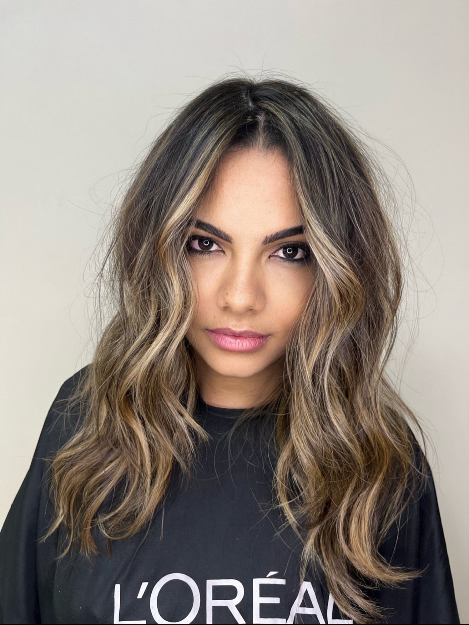 Iluminado com mechas bege contornando o rosto e raiz escura, cabelo médio ondulado