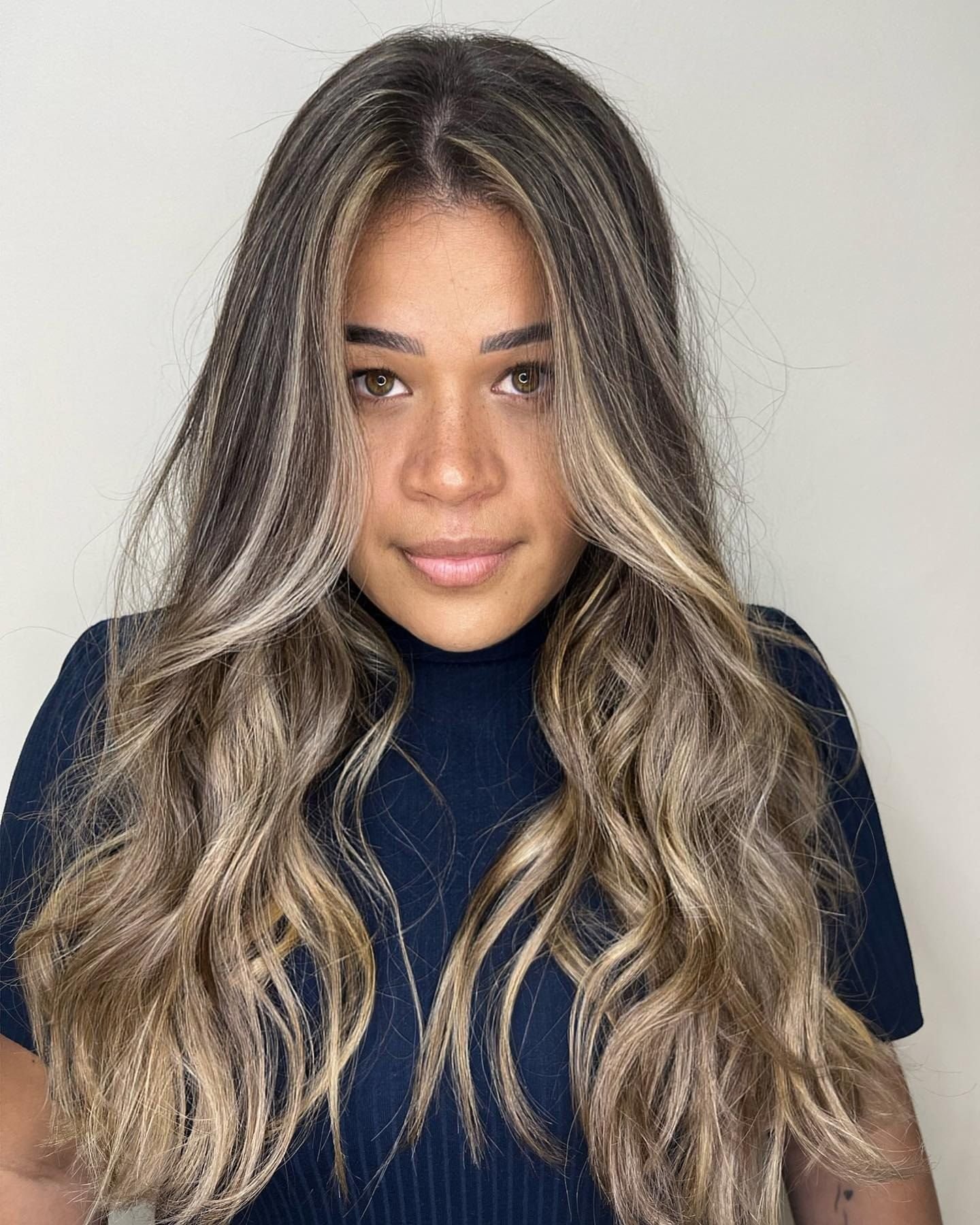 Morena iluminada com mechas claras contornando o rosto, cabelo longo com ondas